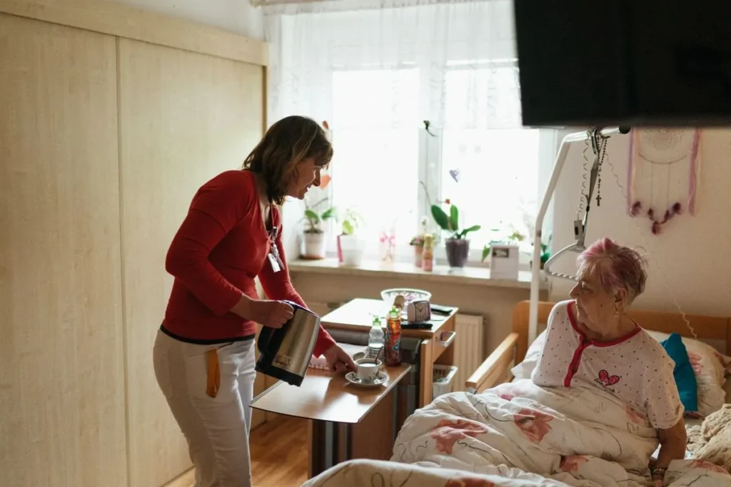 Opiekunka podaje herbatę seniorce w jej pokoju