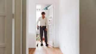Seniorka idzie z balkonikiem przez jasny korytarz w domu - zapobieganie upadkom