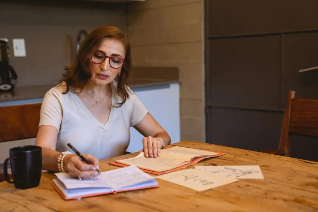 Kobieta zapisuje godziny pracy w zeszycie przy stole