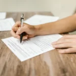 Dłonie wypełniające formularz urzędowy przy stole